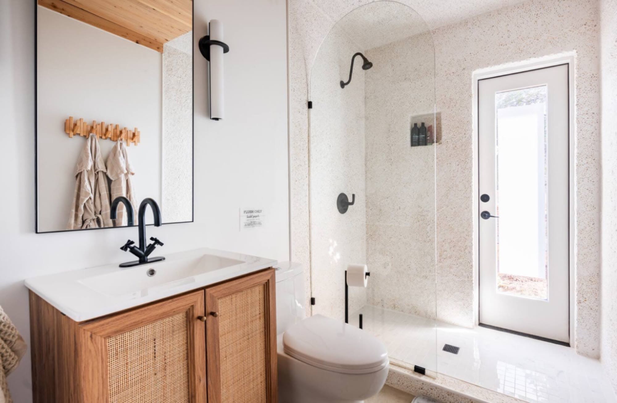 White bathroom with a rattan vanity, black fixtures and a walk-in shower