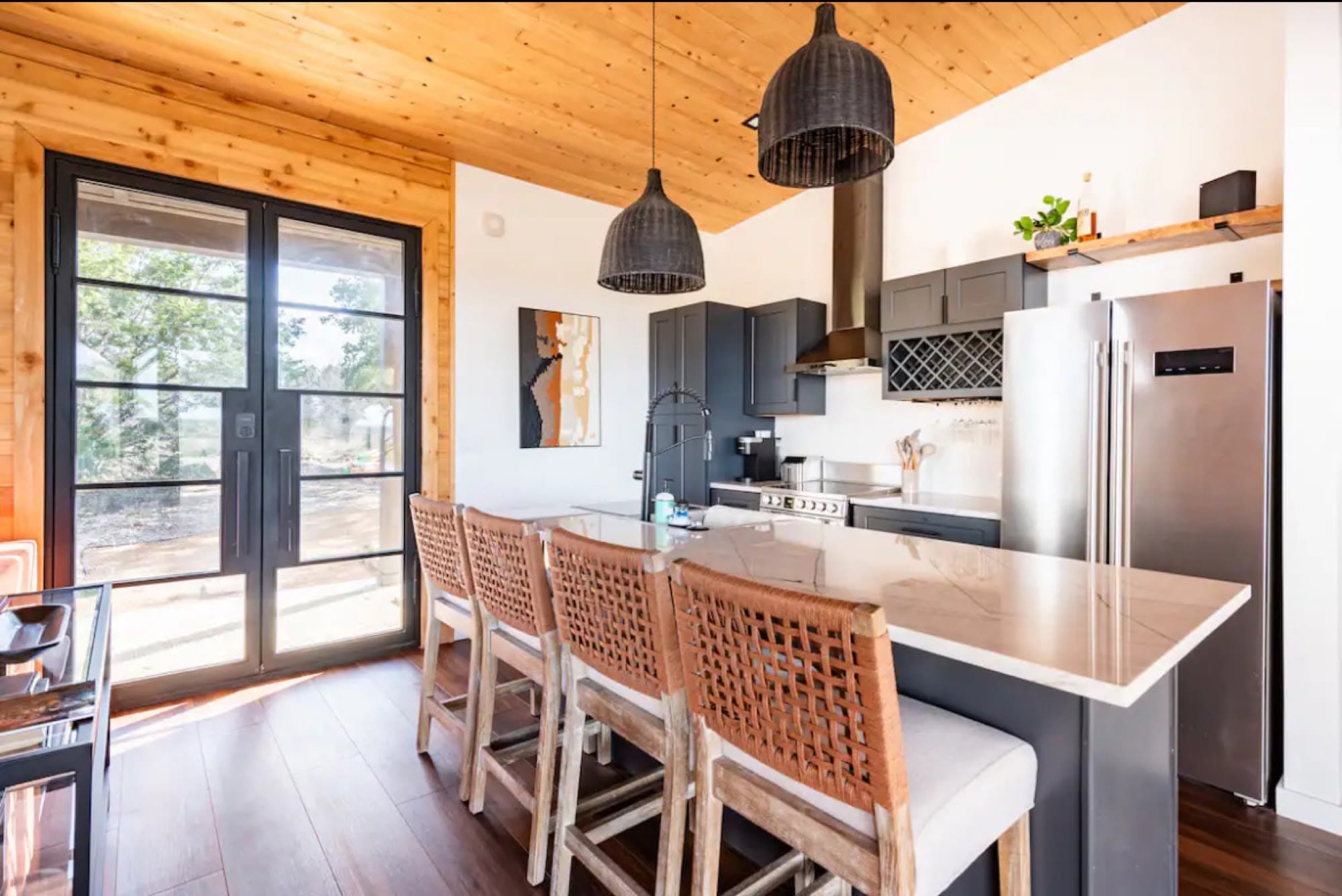 Dining counter with rattan stools beside black-framed glass doors to the porch