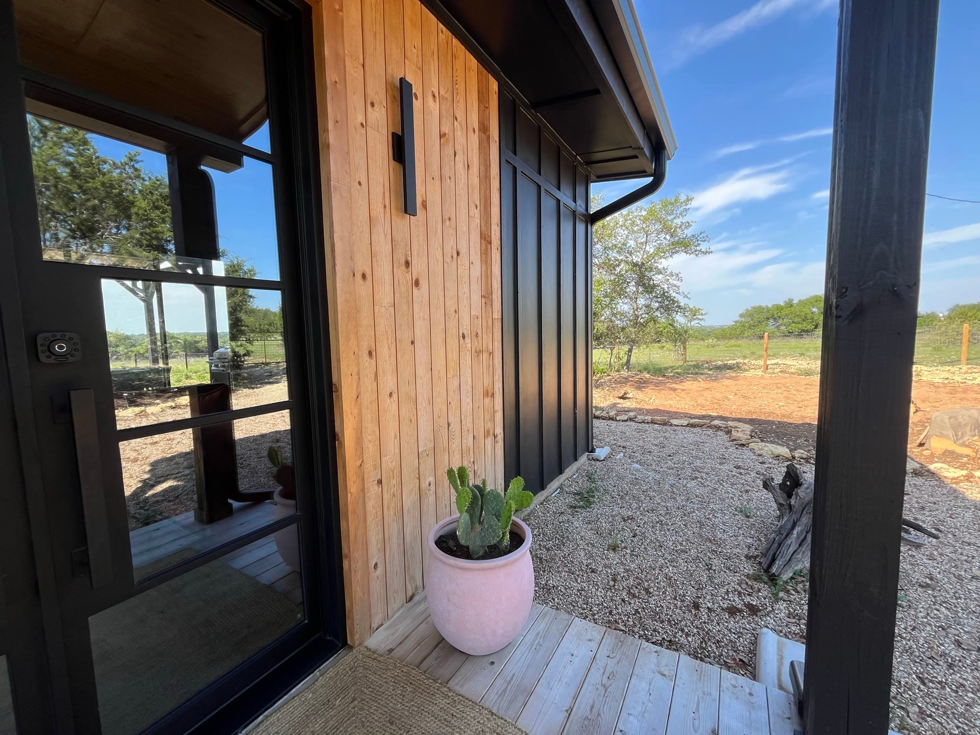 Cedar-clad cabin entry with a black steel door and a potted plant on the deck