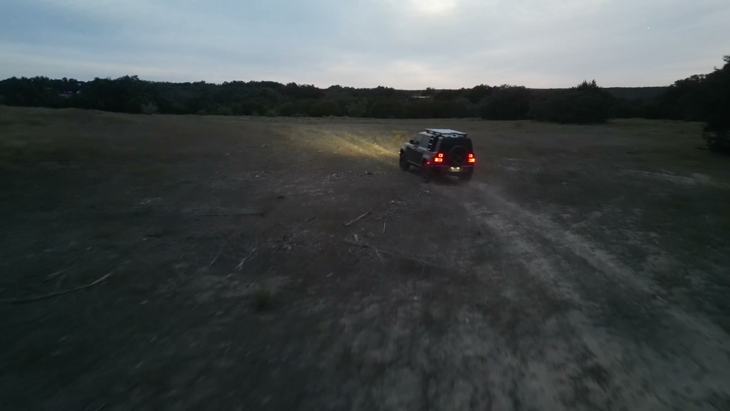 Drone view of an SUV driving away across the pasture at dusk