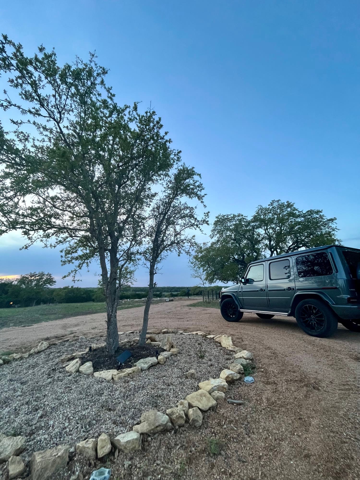 A dark SUV parked beside a live oak on the gravel cabin drive