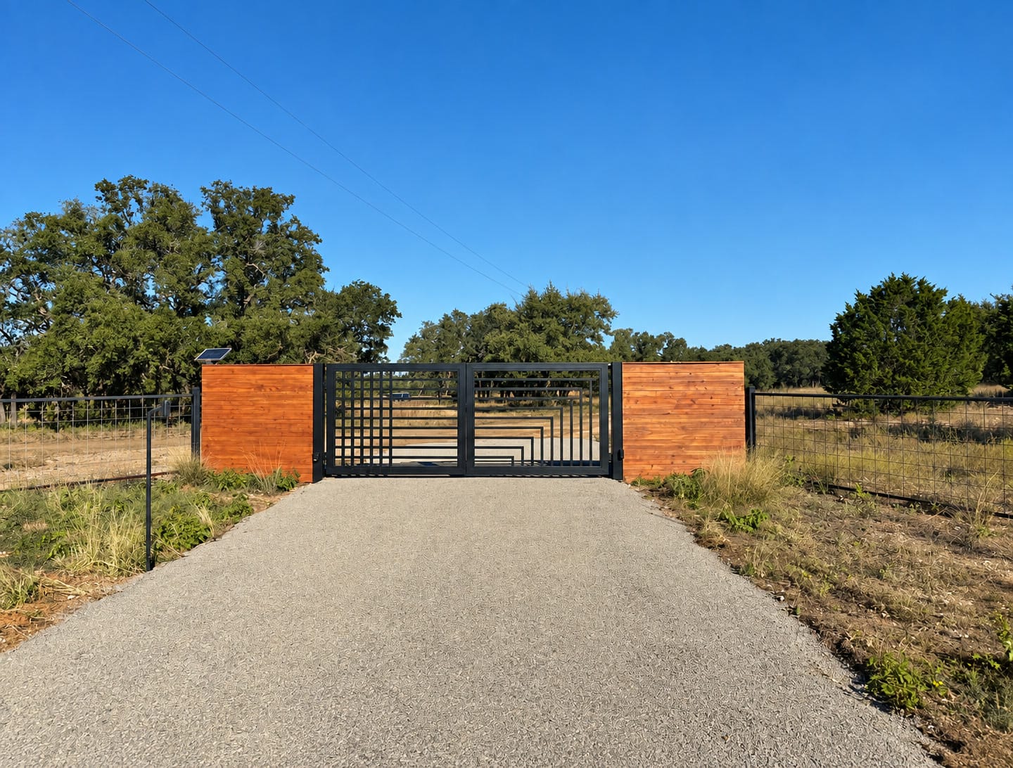 The ranch gate: black steel between two cedar panels at the end of a gravel drive